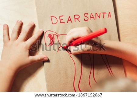 Childs hands drawing letter to Santa close up. Text Dear Santa and picture of dinosaur