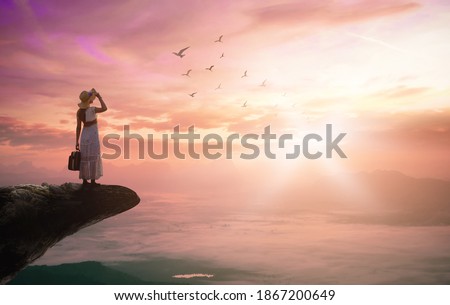 Spiritual Journey concept: Silhouette traveler woman with birds flying on mountain sunset background