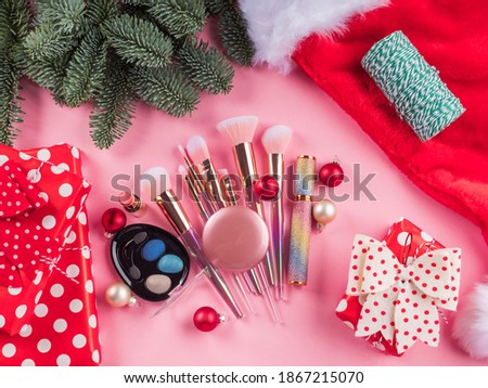 Christmas spruce branches, santa cap and presents with shiny make up tools, products on pink background. Festive beauty gift concept
