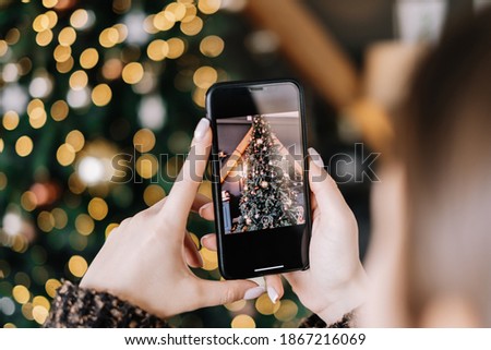 Young woman takes pictures of Christmas tree on smartphone. Close-up