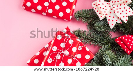 Festive christmas tree fir spruce branch decorated with red and white bows and polka dot wrapped gifts on pink background. Flat lay
