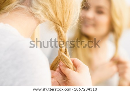Young pretty blonde woman creating her hairstyle, making braid. Lovely female getting ready