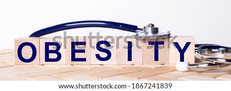 The word OBESITY is written on wooden cubes near a stethoscope on a wooden background. Medical concept