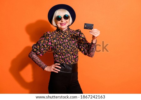 Photo of smiling cheerful positive happy grandmother demonstrate credit card isolated on orange color background