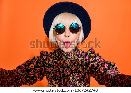 Portrait of old funky cool crazy hipster grandmother take selfie stick tongue out isolated on orange color background Royalty-Free Stock Photo #1867242748