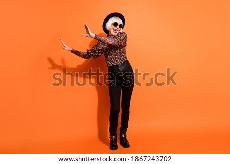 Full size photo of crazy smiling excited happy old lady dancing wear black trousers and glasses isolated on orange color background