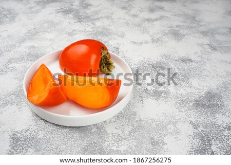 Persimmon slices on white round plate on light gray concrete background. Recipe, vitamin, nutrition concept. Copy space, close-up