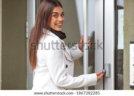 Young business woman in white suit entering code on the intercom keyboard of the residential modern building. Happy woman ringing on doorbell at building entrance. Using intercom.