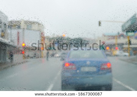 Blurred Car through heavy rain. With water on windshield. Wipers are turned on at high speed. dangerous to drive, blurred colourful light in distance