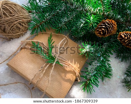 Rustic gift on white snow background with fir branches and pine cones.