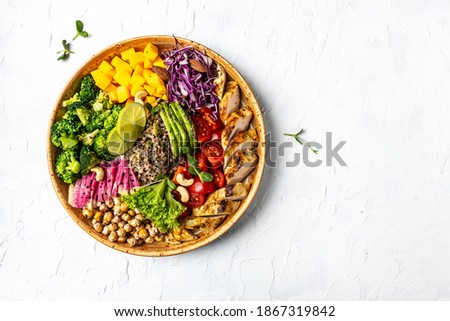 Buddha bowl with kale salad, chicken fillet quinoa, avocado, pumpkin, tomato, broccoli, chickpea, watermelon radish, fresh lettuce salad, nuts, healthy balanced eating for lunch.