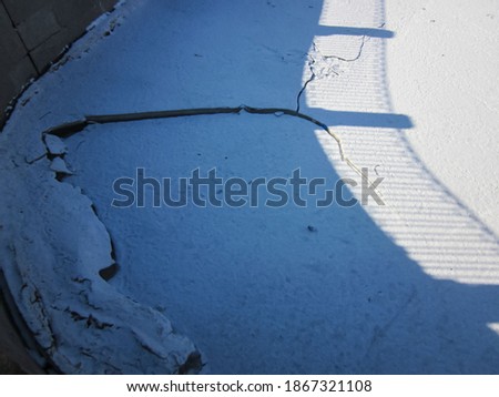 Close-up of the crack in the ice on the river and the shadow of the embankment fence