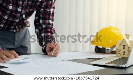 An architect or male engineer working at home drafting a construction project with a laptop and a hat next to it.