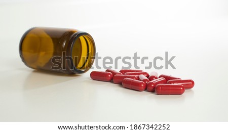 Red antibiotic capsule and brown glass bottle on white background