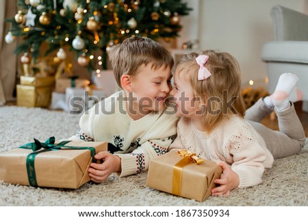 Christmas portrait of adorable little boy and girl. Children open gift boxes near the Christmas tree during winter holidays. Happy kids in cozy clothes.