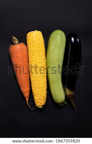 carrots, eggplant, zucchini, corn in a row on a black background