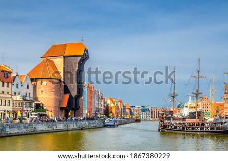 Gdansk cityscape with Zuraw Crane building and typical colorful houses at Long Bridge embankment promenade, medieval wooden ship on Motlawa river water in historical town centre, Pomerania, Poland