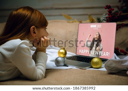 Gifts. Happy caucasian little girl during video call with laptop and home devices, looks dreamful and happy. Talking to Santa before New Year's eve, her family, watching cartoons, typing text. Bokeh