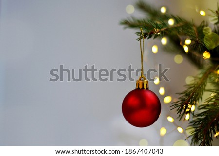 christmas red ball hanging on pine branches with garland on light colored background