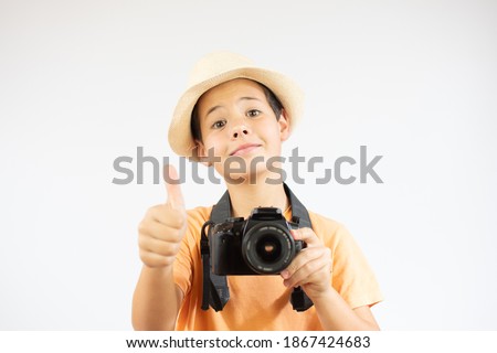 Portrait of a cheerful boy holding a camera with hat and thumb up