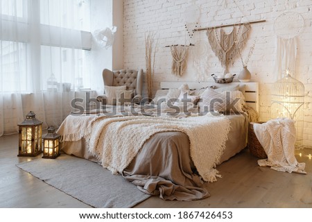 Side view of lovely bedroom with plaid and pillows on comfortable bed, home decor and cushions on soft armchair in white interior design in bohemian style Royalty-Free Stock Photo #1867426453