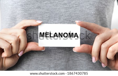 The girl in front of her holds a card with the text of MELANOMA with both hands.