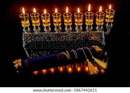 Torah and menorah with burning oil candles with reflection.