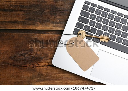 Metal key with blank tag and laptop on wooden table, top view. Keyword concept