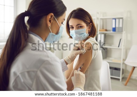 Vaccination, immunization, disease prevention concept. Woman in medical face mask getting Covid-19 or flu vaccine at the hospital. Professional nurse or doctor giving antiviral injection to patient Royalty-Free Stock Photo #1867481188