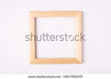 Close up photo of light wooden empty frame hanging on white wall isolated white color background