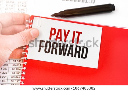 Business man holding a red notebook and white card with text PAY IT FORWARD. Financial concept