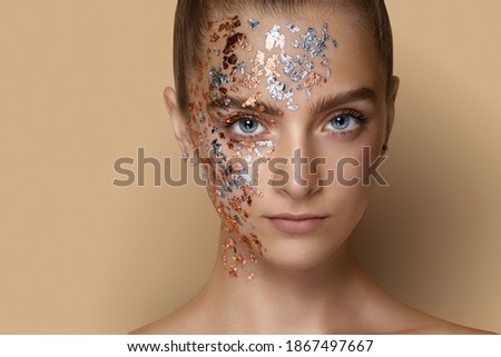 young beautiful girl on a beige background. close-up portrait. The girl looks into the camera. Gold metallic particles on the face