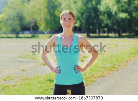 Fitness young smiling woman warming up before exercises in the city park