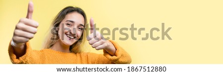 Happy young caucasian female in an orange sweater making thumb up sign and smiling. Good job and respect.	