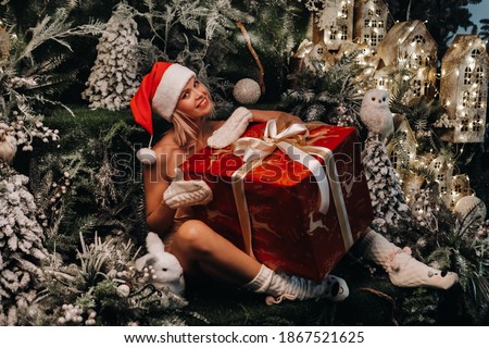 a girl in a Santa hat with a big Christmas gift in her hands on a fabulous Christmas background.Smiling woman in a bathing suit on the background of Christmas trees and small houses