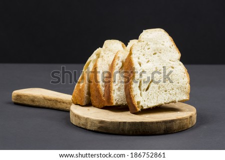 Still life composition with wooden kitchen cutting board and slices of bread  on dark background