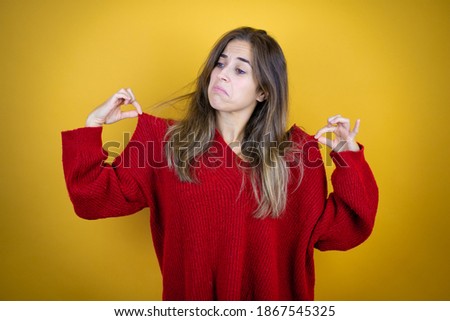 Young beautiful woman wearing red sweater over isolated yellow background holding her t-shirt with a successful expression