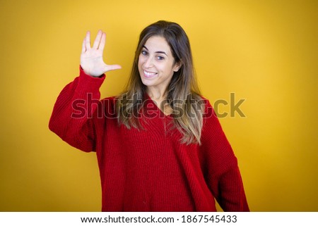 Young beautiful woman wearing red sweater over isolated yellow background doing hand symbol