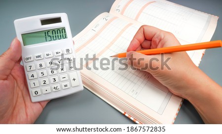 Close up of household account book. Asian woman taking notes in household account book while calculating Royalty-Free Stock Photo #1867572835
