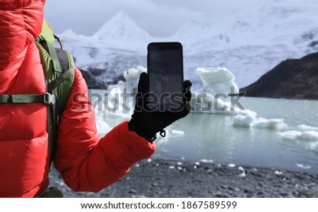 Woman hiker taking photo of glacier with smartphone in winter