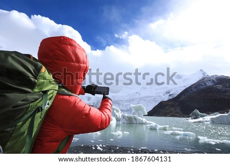 Woman hiker taking photo of glacier with smartphone in winter 