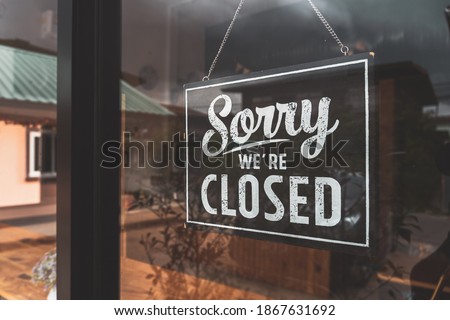 " Sorry we're closed " sign in black and white, on shop glass door.