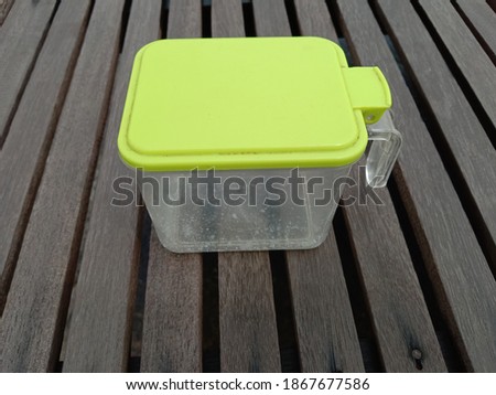A plastic box for spices lies on wooden brown plank.