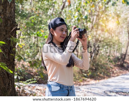 Pretty Asian young woman enjoys using camera taking photos in the forest while camping or hiking.