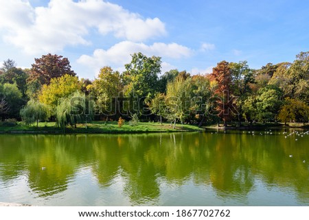 Landscape with many large green and yellow old trees near the lake in Carol Park in Bucharest, Romania,  in a sunny autumn day