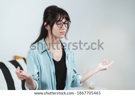 Full length woman making mudra gesture, sitting in lotus position on comfortable couch at home. Peaceful millennial female deeply meditating, doing breathing yoga exercises alone.