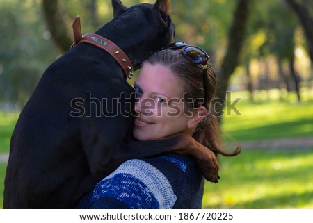 A young woman on a walk with a Doberman is enjoying talking with a pet. Selective focus with blurred background. Shallow depth of field.