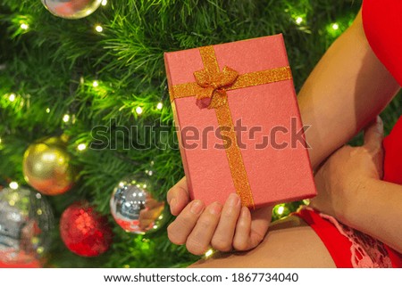 Women in red dress hands holding red box for giving someone for christmas day, women standing by the christmas tree.