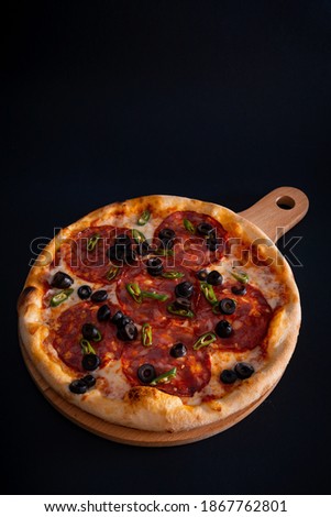 A closeup of a freshly baked cheesy pizza with salami, olives, and pepper on a wooden tray
