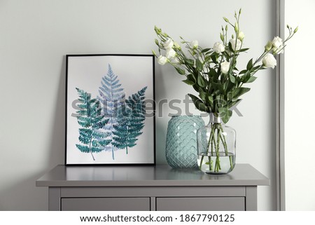 Composition with eustoma flowers in glass vase on grey cabinet indoors